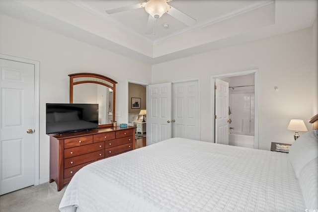 bedroom with ornamental molding, light colored carpet, ensuite bathroom, a ceiling fan, and a raised ceiling