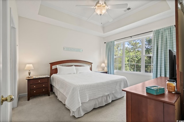 bedroom featuring light carpet, crown molding, a tray ceiling, a ceiling fan, and baseboards