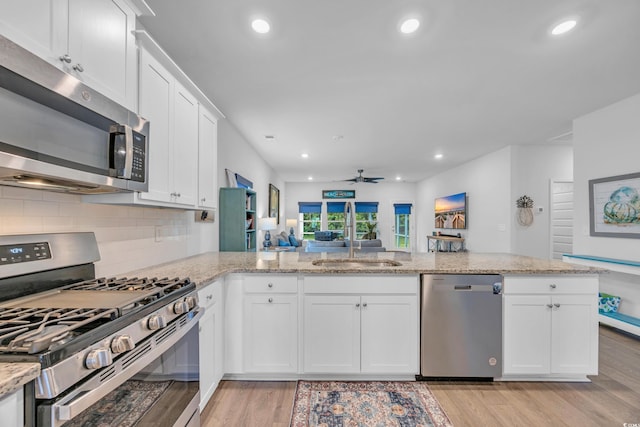 kitchen with appliances with stainless steel finishes, light wood-type flooring, tasteful backsplash, white cabinets, and light stone counters