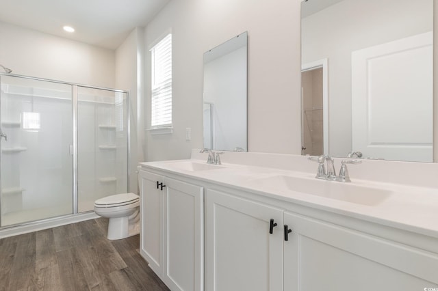 bathroom featuring a shower stall, wood finished floors, toilet, and double vanity