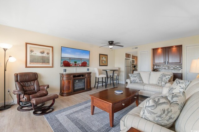 7509 N Ocean Blvd Unit 404, Myrtle Beach, SC 29572 - living room with light wood-type flooring, a ceiling fan, a glass covered fireplace, and baseboards