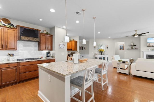1035 Brentford Pl, Myrtle Beach, SC 29579 - kitchen featuring premium range hood, gas stovetop, brown cabinets, a center island with sink, and light stone counters