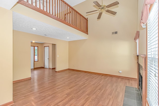 934 Tiffany Ln, North Myrtle Beach, SC 29582 - unfurnished living room featuring a fireplace with flush hearth, light wood-style flooring, ceiling fan, baseboards, and a towering ceiling