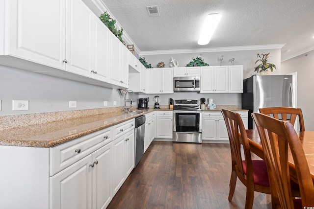 kitchen with appliances with stainless steel finishes, ornamental molding, a sink, white cabinetry, and dark wood finished floors