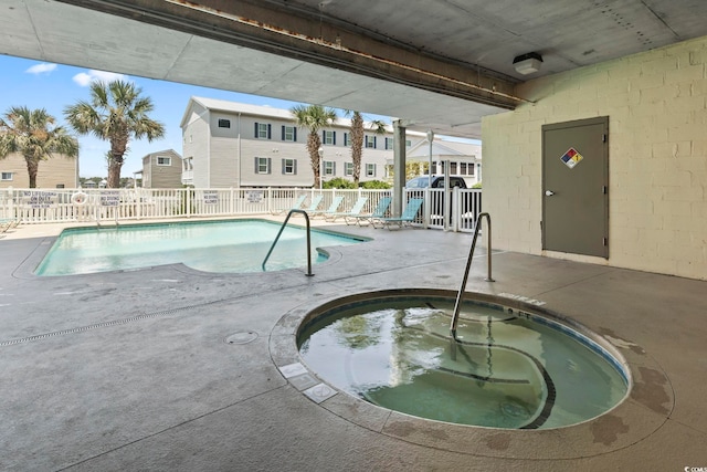 community pool featuring fence, a hot tub, a patio area, and a residential view