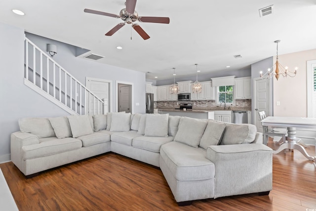 living area featuring a chandelier, dark wood-style flooring, a ceiling fan, recessed lighting, and stairs