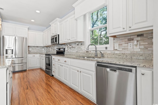 kitchen with appliances with stainless steel finishes, a sink, white cabinetry, tasteful backsplash, and light stone counters