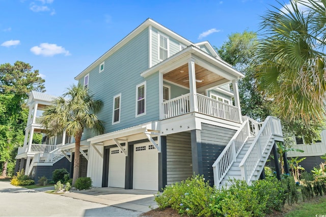 raised beach house with stairway, a garage, driveway, ceiling fan, and covered porch