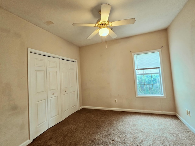 unfurnished bedroom with dark colored carpet, a closet, baseboards, and a ceiling fan