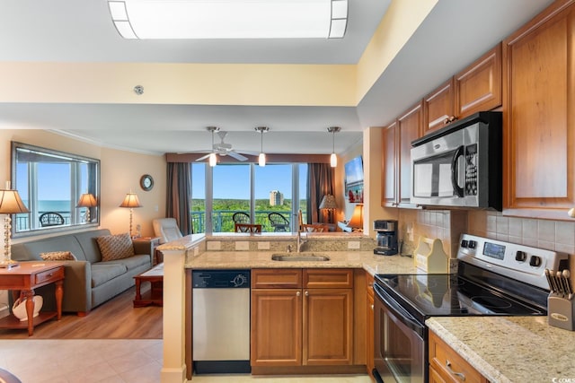 kitchen featuring stainless steel appliances, a sink, brown cabinetry, open floor plan, and a peninsula