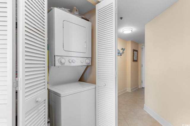 laundry room featuring stacked washing machine and dryer, light tile patterned floors, and baseboards