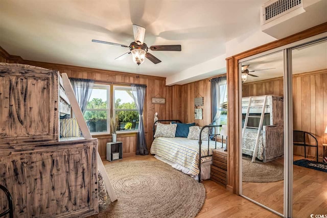 bedroom featuring wooden walls, light wood-style floors, a ceiling fan, and multiple closets