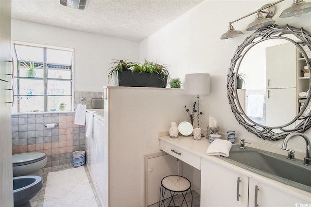bathroom with a bidet, a textured ceiling, toilet, tile walls, and vanity