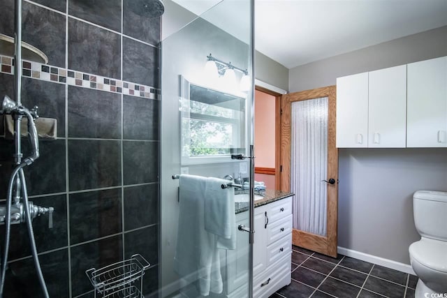 bathroom featuring toilet, tiled shower, tile patterned floors, vanity, and baseboards
