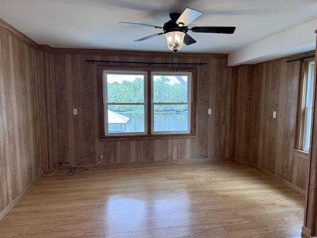 spare room featuring light wood-style floors, wood walls, a ceiling fan, and baseboards