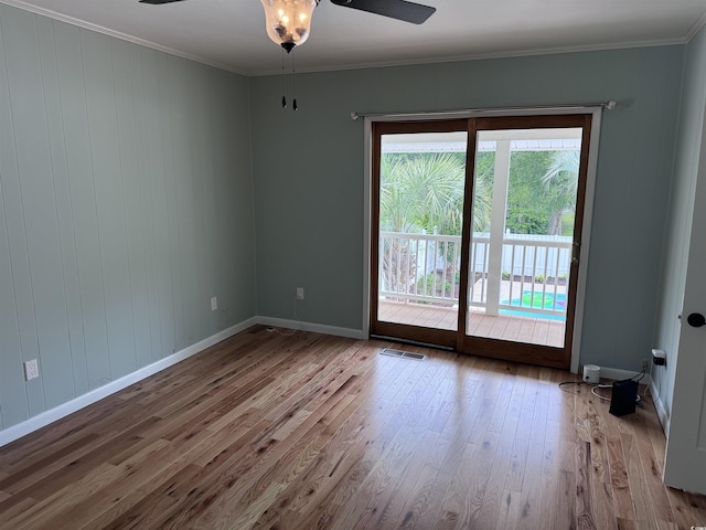 empty room with wood finished floors, a ceiling fan, baseboards, and crown molding