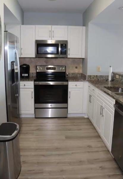 3000 Ocean Blvd N Unit 508, Myrtle Beach, SC 29577 - kitchen featuring appliances with stainless steel finishes, white cabinets, light wood-style flooring, dark stone counters, and a sink