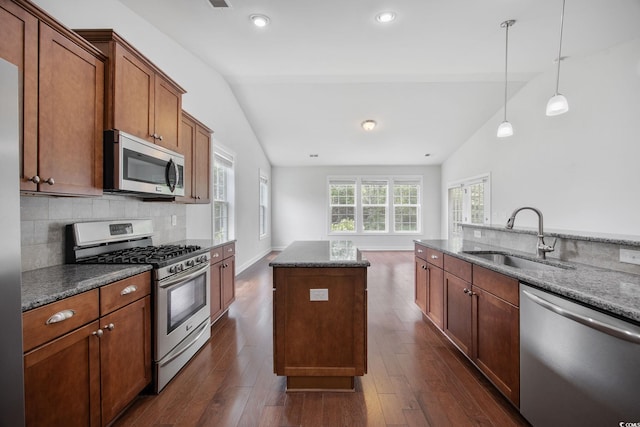 kitchen featuring stainless steel appliances, a sink, vaulted ceiling, backsplash, and hanging light fixtures
