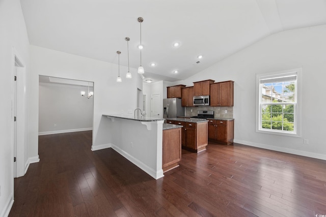 kitchen featuring appliances with stainless steel finishes, vaulted ceiling, a peninsula, a kitchen bar, and brown cabinets