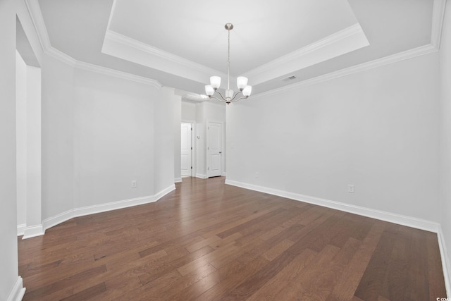 empty room with a tray ceiling, a chandelier, dark wood finished floors, baseboards, and crown molding