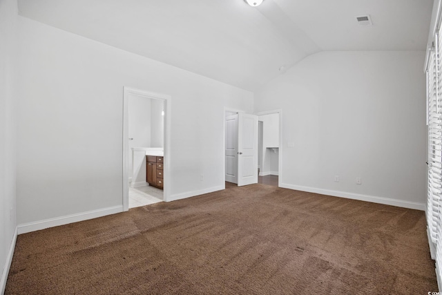 unfurnished bedroom with lofted ceiling, a spacious closet, light carpet, ensuite bathroom, and baseboards