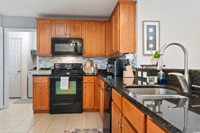 kitchen featuring black appliances, a sink, dark stone countertops, and brown cabinetry