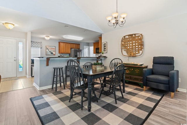 dining area with a chandelier, light wood-style floors, vaulted ceiling, and baseboards