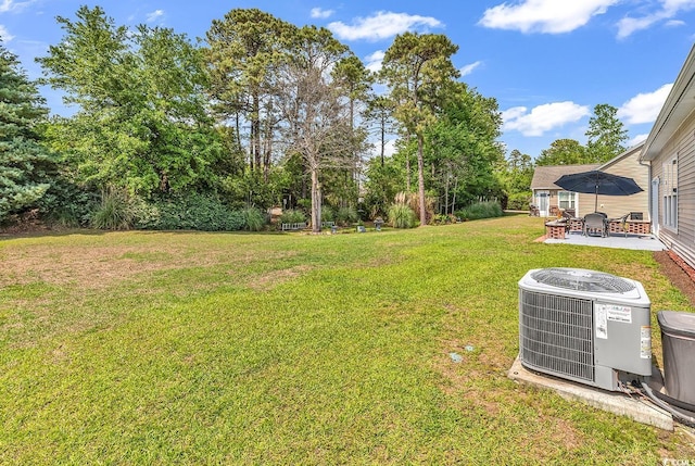 view of green lawn with central air condition unit, a patio area, and view of wooded area