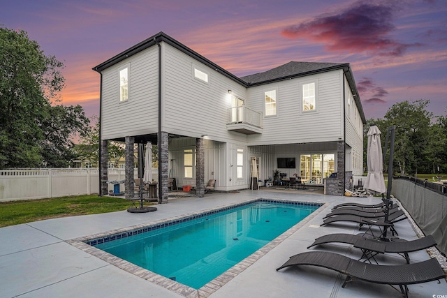 back of house at dusk with a patio area, a balcony, and a fenced backyard