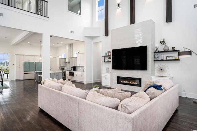 living area with dark wood-type flooring, a glass covered fireplace, baseboards, and a high ceiling