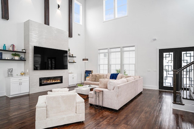 living room with a high ceiling, dark wood-type flooring, a glass covered fireplace, baseboards, and stairway