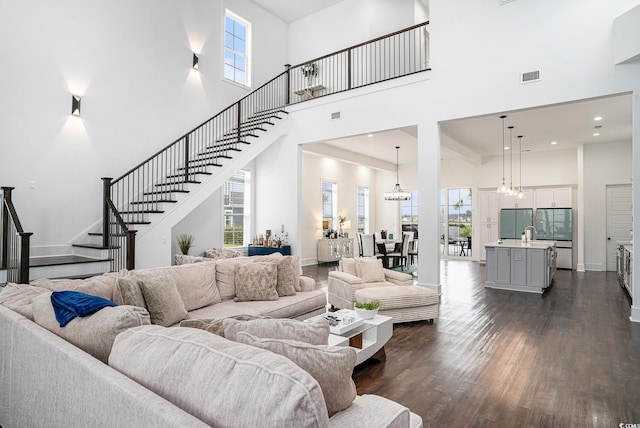 living area with a high ceiling, stairs, plenty of natural light, dark wood-style floors, and a chandelier