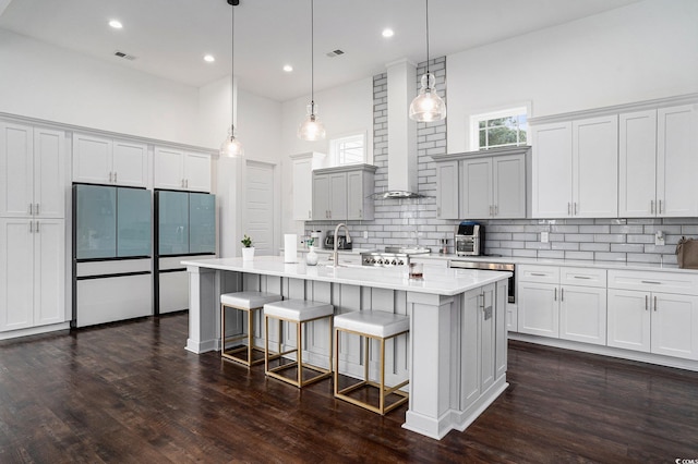 kitchen featuring refrigerator, tasteful backsplash, light countertops, dark wood-style flooring, and a kitchen bar
