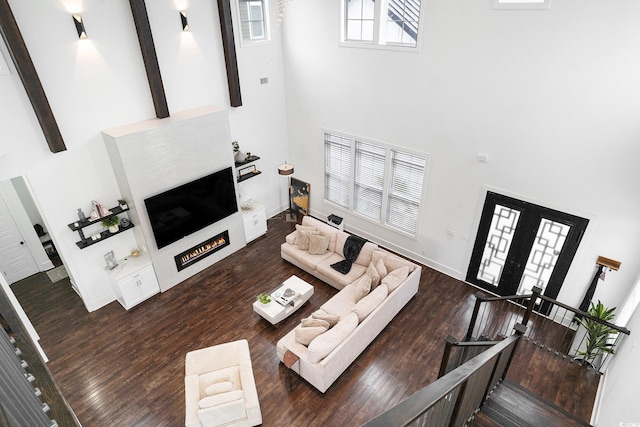 living area featuring a high ceiling, a lit fireplace, wood finished floors, and baseboards