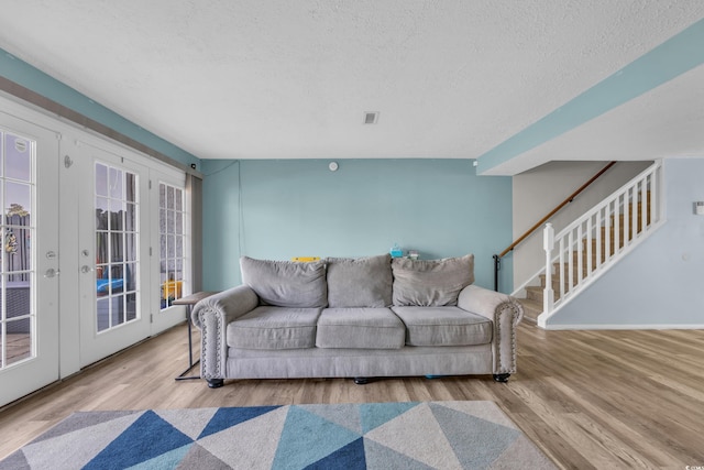 living room featuring french doors, a textured ceiling, wood finished floors, and stairs
