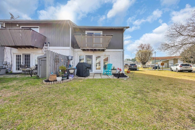 rear view of house featuring french doors, a balcony, a lawn, and a patio