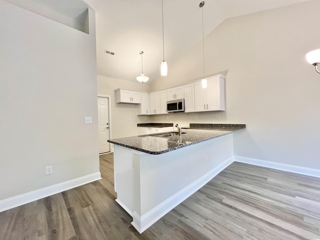 2593 Main St, Loris, SC 29569 - kitchen with stainless steel microwave, a peninsula, high vaulted ceiling, baseboards, and dark stone counters
