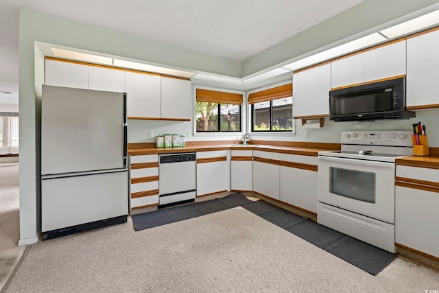 kitchen featuring white appliances, white cabinets, carpet floors, and a sink