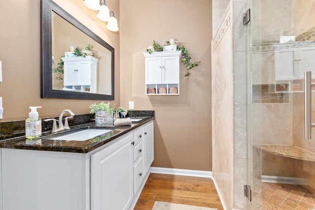 full bath with a shower stall, double vanity, baseboards, and wood finished floors