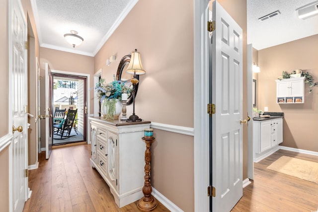 hallway featuring a textured ceiling, light wood-style flooring, crown molding, and baseboards