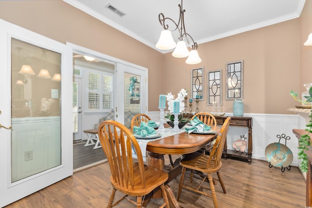 dining space featuring wainscoting, ornamental molding, wood finished floors, and a decorative wall