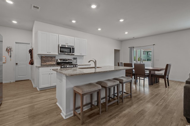 kitchen with appliances with stainless steel finishes, a sink, a breakfast bar, light wood-style flooring, and recessed lighting