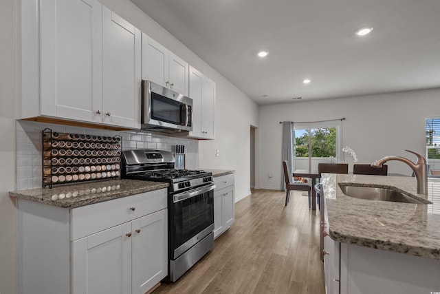 kitchen with stainless steel appliances, a sink, decorative backsplash, recessed lighting, and white cabinets