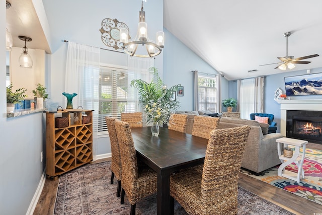 dining room featuring wood finished floors, a chandelier, ceiling fan, a lit fireplace, and baseboards