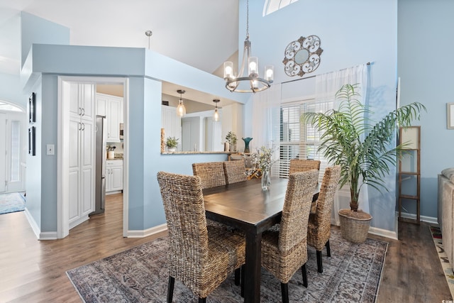 dining area with a towering ceiling, wood finished floors, a chandelier, and baseboards