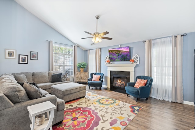 living area featuring ceiling fan, wood finished floors, a lit fireplace, high vaulted ceiling, and baseboards