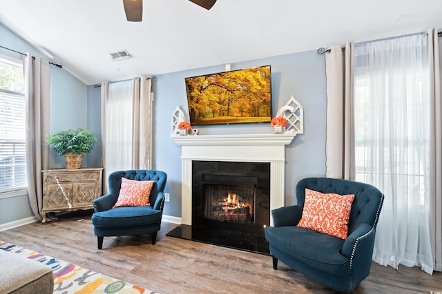 sitting room with vaulted ceiling, a ceiling fan, wood finished floors, a lit fireplace, and baseboards
