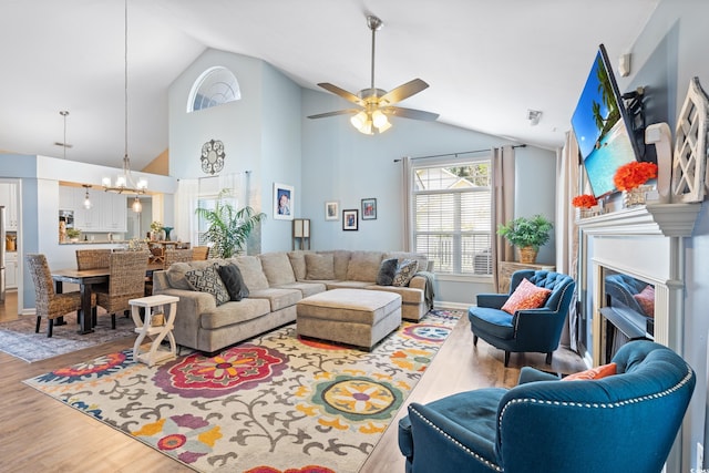 living room with a fireplace, wood finished floors, a chandelier, a ceiling fan, and high vaulted ceiling