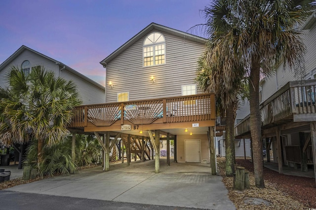 back of house at dusk featuring a carport, driveway, and a wooden deck