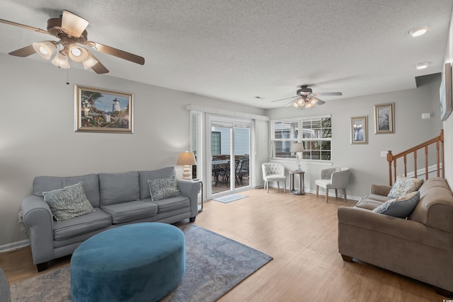 living room featuring a ceiling fan, a textured ceiling, wood finished floors, stairway, and baseboards